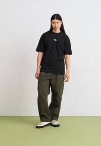 Svart bomulls t-skjorte med en liten grå logo, kombinert med løse olivengrønne cargo-bukser og hvite sneakers med svarte såler.