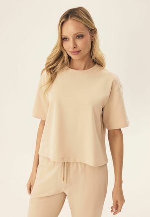 Short-sleeve, cropped t-shirt in light beige cotton, featuring a round neckline and soft texture. Paired with coordinating beige pants.
