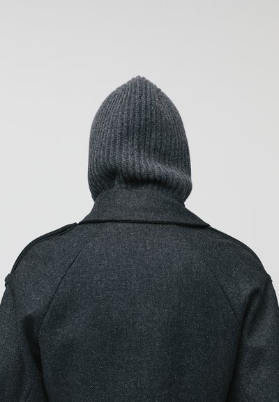 Cappotto di lana grigio scuro con colletto strutturato e distintivo yoke posteriore, abbinato a un cappuccio a costine grigio scuro di maglia.