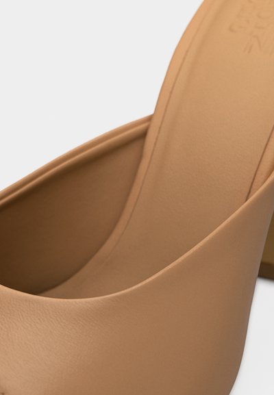 Gros plan d'une chaussure à talon haut en cuir marron clair, mettant en valeur la partie intérieure incurvée et une partie de la semelle intérieure rembourrée.