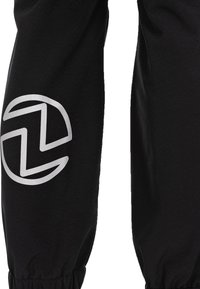 Zwarte stoffen broek met een taps toelopend ontwerp. Heeft een zilveren logo op het linkerkuit. Elastische boorden bij de enkels en een soepele textuur.