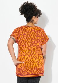 Top de manga corta en naranja con patrón de rayas de tigre en color marrón, con un corte relajado, dobladillo redondeado y un ribete sólido acanalado en el cuello.