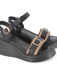 Sandalias de cuña negras con una banda de acento trenzada, detalles de hebilla metálica y correas cruzadas en el tobillo sobre una suela gruesa y texturizada.