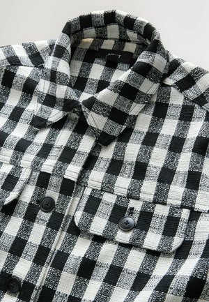 Rutig skjorta i svart och vitt, tillverkad av texturerat tyg. Har krage, två framfickor och svarta knappar.