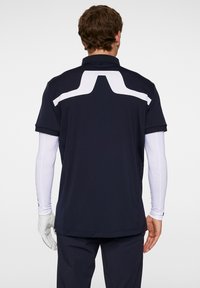 T-paita lyhyillä hihoilla, tummansininen, valkoisella korostussuunnittelulla selässä. Klassinen kaulus ja hengittävä materiaali mukavuutta varten.