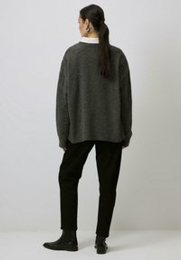 Överdimensionerad grå stickad tröja med ribbad nederkant, bärs över en vit skjorta med krage, i kombination med svarta byxor och ankelboots.