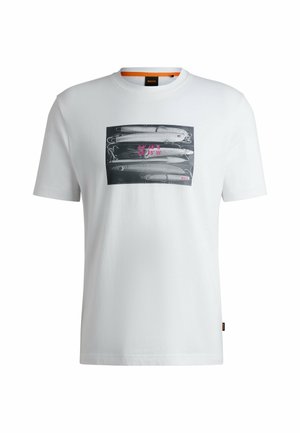 T-shirt bianco in cotone con una grafica in bianco e nero di esche da pesca, con testo rosa e una piccola etichetta logo sull'orlo.