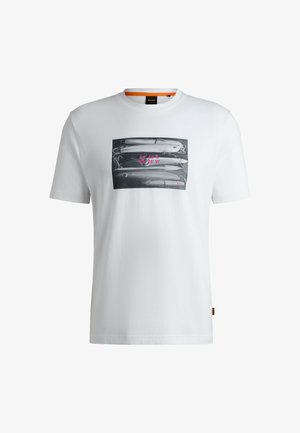 T-shirt bianco in cotone con una grafica in bianco e nero di esche da pesca, con testo rosa e una piccola etichetta logo sull'orlo.