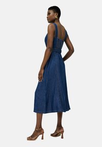 Vestido midi de mezclilla con tirantes anchos, corsé ajustado, cintura ceñida con cinturón y un dobladillo fluido. El color es azul oscuro con una textura suave.