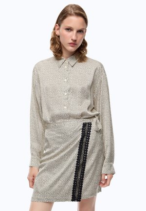 Mujer que lleva un vestido beige de manga larga con pequeños lunares negros y una raya vertical de encaje negro en la sección de la falda.