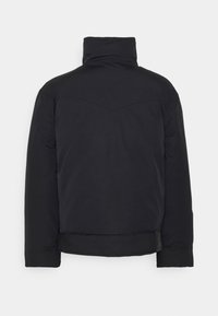 Svart vadderad jacka, hög krage och en något kortad silhuett. Har en jämn, matt yta med ton-i-ton sömmar och ingen synlig hårdvara.