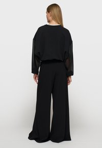Czarna, oversize bluza z przezroczystymi rękawami oraz szerokimi czarnymi spodniami. Miękka faktura, luźny krój i prosta konstrukcja bez wzorów.