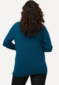 Mėlynas megztinis su ilgomis rankovėmis, apvaliu iškirpimu ir šoninėmis išpjovomis apdailoje, rodomas iš nugaros šviesiame fone.