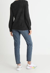 Maglione nero a trama, jeans blu con orlo sfilacciato e sneaker bianche con dettagli multicolore. Vista da dietro.