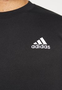 T-shirt in cotone nero con logo Adidas ricamato in bianco sul petto. Collo rotondo semplice e maniche corte.