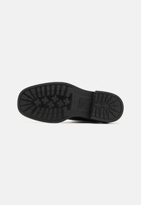 Black rubber sole with a textured grip pattern and rugged design. Rounded toe with a reinforced heel for added durability.