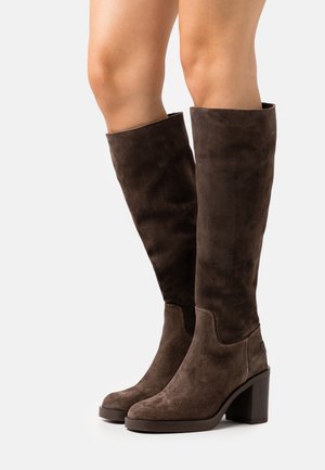 Botas altas hasta la rodilla de ante marrón con tacón cuadrado, textura suave, punta redondeada y diseño sin costuras con un cuello ligeramente levantado.