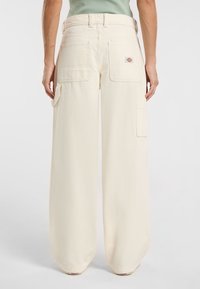 Pantaloni cargo a gamba larga in morbido tessuto crema; presenta ampie tasche laterali e posteriori, passanti per cintura rinforzati e una piccola etichetta con logo.