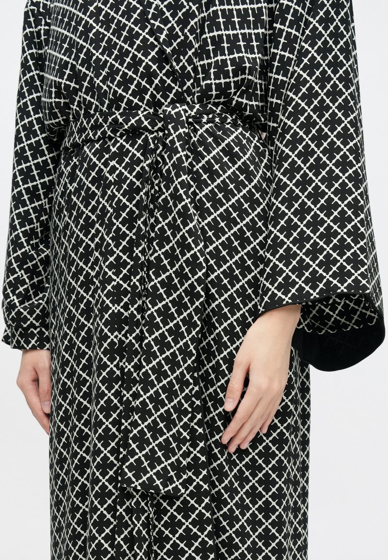 Schwarz-weißer, gemusterter Morgenmantel mit Wickeldesign, ausgestattet mit einem Bindegürtel, weiten Ärmeln und einem Rautenmuster mit sich schneidenden Linien.