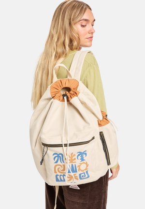 Sac à dos en toile beige avec fermeture à cordon, accents orange, poche zippée à l'avant et motif bleu et orange sur le devant.