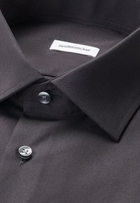 Chemise noire habillée avec col classique et deux boutons noirs, avec une étiquette blanche portant le nom de la marque "seidensicker" à l'intérieur du col.