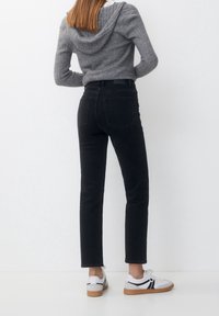 Sudadera de punto acanalado gris con capucha, combinada con jeans negros de pierna recta y zapatillas blancas con acentos negros y suela beige.
