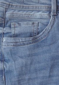 Närbild av ljusblå denimjeansficka med detaljerad sömnad och en liten myntficka inne i den främre högra fickan.