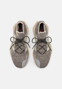 Zapatillas deportivas ligeras con parte superior de punto gris, acentos beige y suelas de goma texturizadas. Presentan cordones redondos y una construcción duradera.