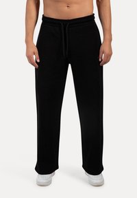 Sorte bomulds sweatpants med snøre i taljen, bred benlængde og glat tekstur. Bæres med hvide sneakers for kontrast.