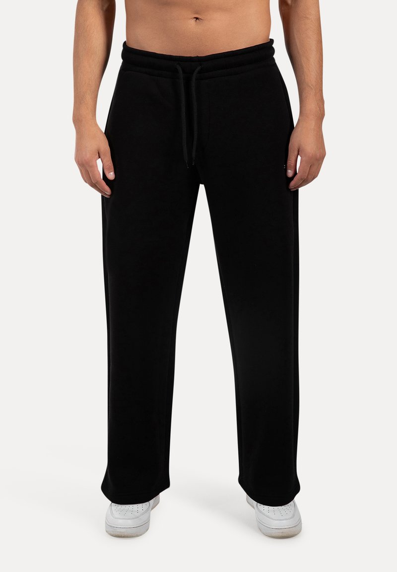 Sorte bomulds sweatpants med snøre i taljen, bred benlængde og glat tekstur. Bæres med hvide sneakers for kontrast.