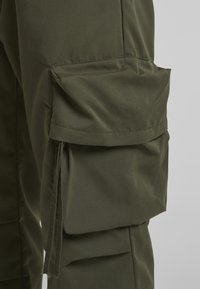 Pantalones cargo en verde olivo, con un gran bolsillo lateral, textura suave y tela resistente con detalles de costura visibles.