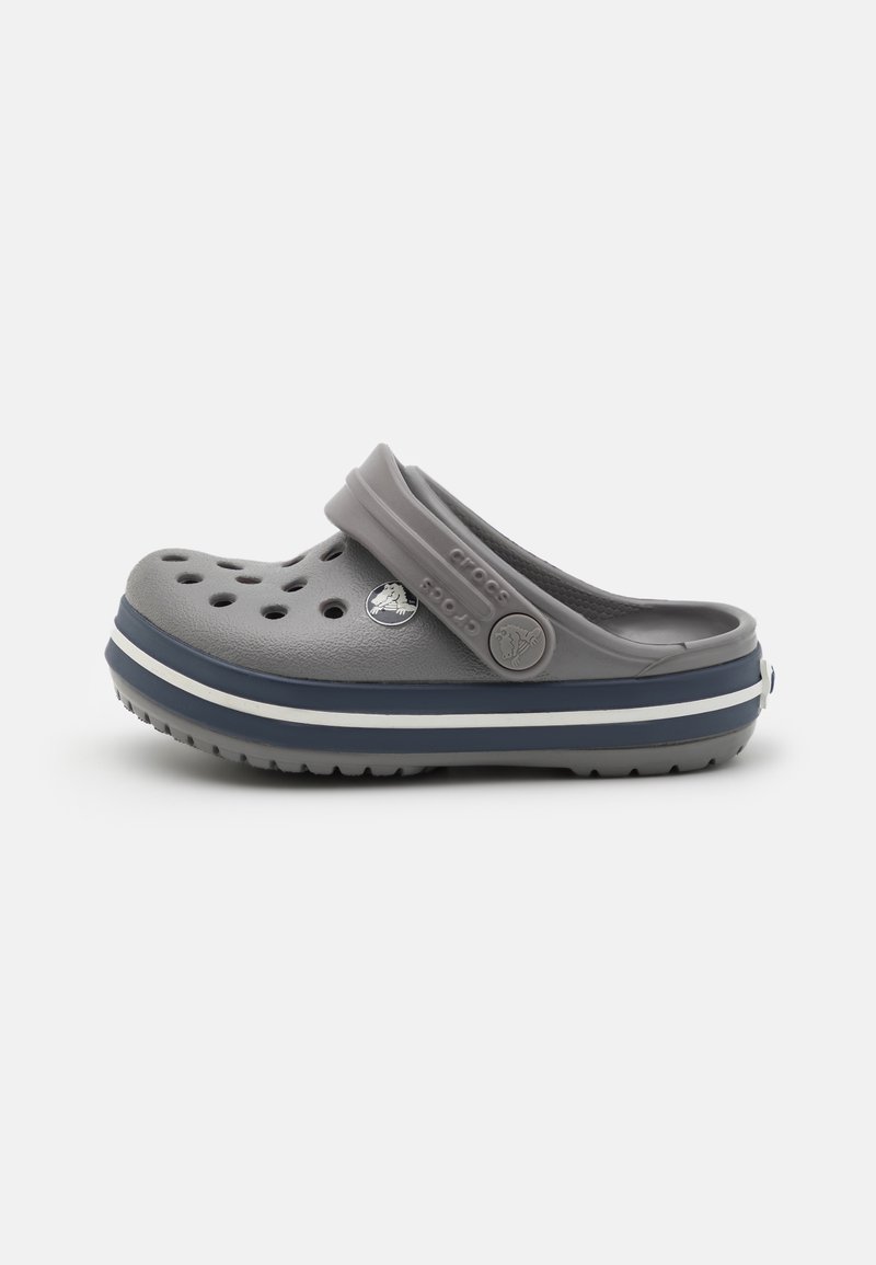 Sabot gris à enfiler avec des trous de ventilation, bride de talon réglable et semelle rayée bleu marine et blanche, conçu pour un usage décontracté.