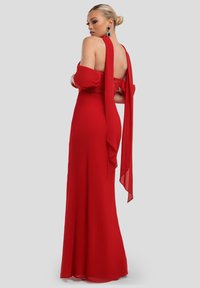 Červené šaty až na zem z hladké látky s krajkovým živůtkem, odhaleným zadním dílem a volnými rukávy. Výrazná barva a elegantní designové detaily.