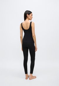Débardeur noir et leggings ajustés en tissu extensible, avec un dos échancré. Design simple avec une texture lisse. Sans motifs ni accents.