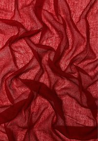 Red translucent fabric with soft folds and wrinkles creating abstract flowing patterns and shadows.