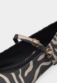 Ploché topánky s čiernymi a béžovými zebrovými pruhmi, vybavené tenkým remienkom a ozdobou v podobe pracke v zlatom tóne na hornej časti.