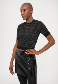 Maglione cropped nero con un pattern testurizzato di lettere intrecciate, abbinato a una gonna nera lucida e collant neri.