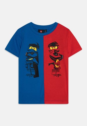 Dziecięca koszulka z krótkim rękawem, w połowie niebieska i w połowie czerwona, z dwoma postaciami LEGO ninja w pasujących kolorach z założonymi ramionami.