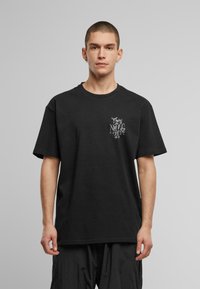 Black cotton t-shirt with short sleeves, featuring a white graphic on the left chest area. Loose fit, crew neckline, smooth texture.