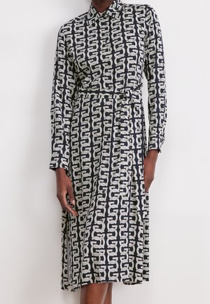 Robe longue à manches longues noir et blanc avec motif géométrique en forme de maillons de chaîne, col boutonné et ceinture à nouer assortie à la taille.