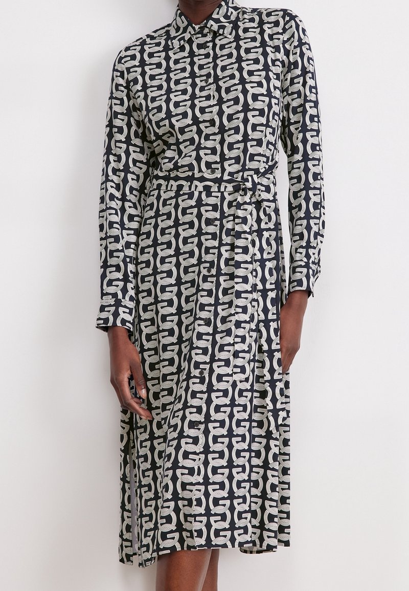 Robe longue à manches longues noir et blanc avec motif géométrique en forme de maillons de chaîne, col boutonné et ceinture à nouer assortie à la taille.