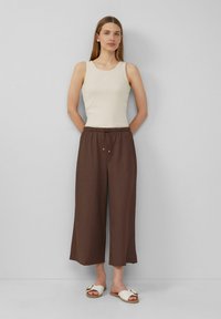 Débardeur en ribbed crème et pantalons larges marron avec une taille élastique. Sandales blanches à glissière avec un accent décoratif en métal.