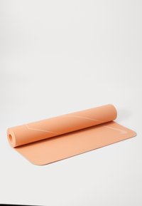 Yogamat u mekom breskvi, izrađena od teksturiranog materijala, djelomično smotana s bijelim naglaskom i logotipom na površini.