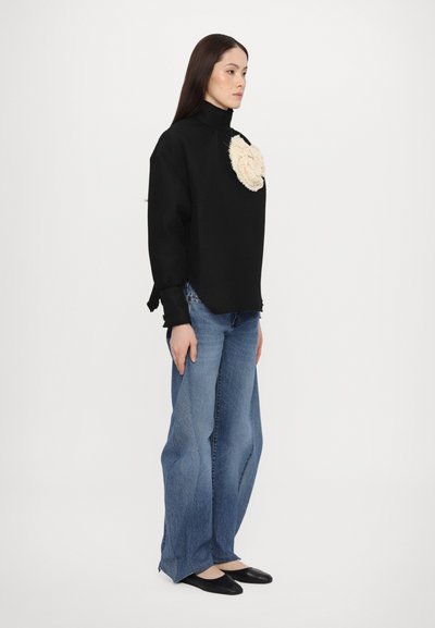 Maglione nero a maglia waffle con un accento floreale beige testurizzato, abbinato a jeans in denim blu a gamba larga e scarpe flat nere.