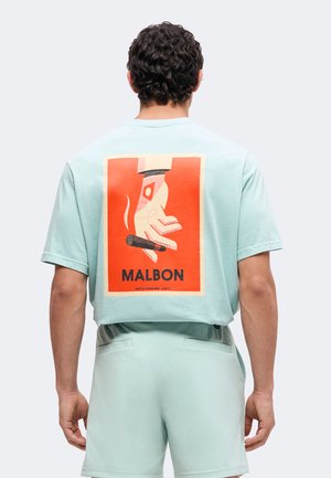 Mand iført lyseblå skjorte og shorts, bagfra med en grafik af en hånd, der holder en cigar på orange baggrund med ordet "MALBON."