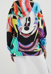 Färgglad grafisk hoodie med en stor leende karaktär på baksidan och livliga geometriska mönster i rött, blått, grönt och svart.