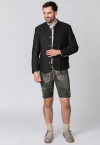 Traditional Bavarian outfit featuring a dark wool jacket with wooden buttons, grey leather shorts with embroidery, and beige knee-high socks.