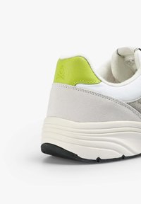 Sneaker grigia e bianca con un accento verde lime sul tallone, realizzata in materiale scamosciato, con una suola spessa e imbottita e dettagli testurizzati sul tallone.