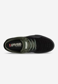 Zapatilla de skate de ante negro con acentos en verde oliva, que presenta una puntera texturizada, cordones planos y una plantilla con marca. Detalles de costura visibles.