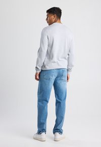Maglione grigio a collo rotondo con maniche lunghe, abbinato a jeans azzurri chiari e sneaker bianche, visto da dietro. Sottile texture sul maglione.
